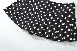 Vue détaillée d'une mini-jupe plissée noire à pois blancs avec d'élégants plis accordéon