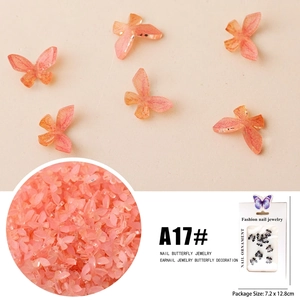 Macro detail of gradient orange-pink butterfly nail charms with glitter and packaging