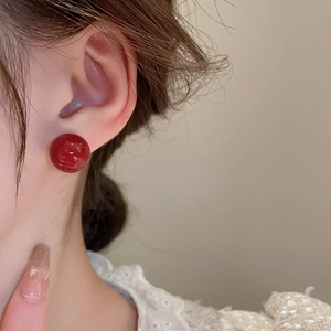 Detailed view of model wearing shiny red spherical stud earrings with gold plating