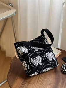 Close-up of white butterfly embroidery and 'simple wish' label on black canvas bag
