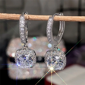 Macro shot of square-cut zircon drop earrings with halo setting on a wood branch