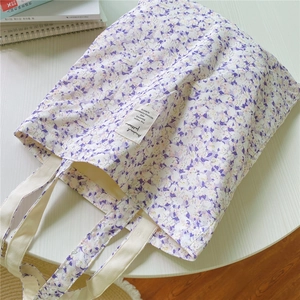 Detail shot of purple floral canvas tote bag featuring an ivory strap and chic woven label