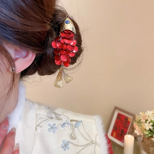 Detailed close-up of fish-shaped hair clip with red sequins and gold metallic accents