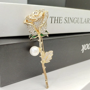 Macro shot of gold rose brooch with sparkling crystals, green enamel, and white pearl