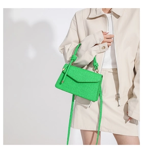 Detail of green woven crossbody bag with knotted handle and textured flap closure