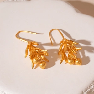 Detail of matte gold leaf earrings with small bead charms on a white stone background