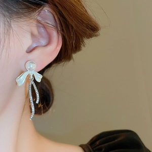 Detail of luxury pearl earring with bow and rhinestone tassel on model ear