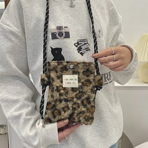 Detail view of leopard print plush crossbody bag with woven strap and branded cloth label
