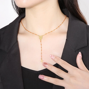 Detail of bohemian gold y-necklace with orange resin beads and a cross pendant on a model