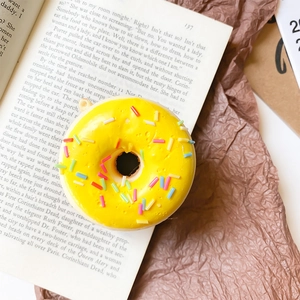 Close-up of yellow 3D donut phone grip with colorful sprinkles on a vintage book