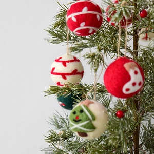 Handmade wool felt Christmas ball ornaments with festive patterns hanging on pine branches