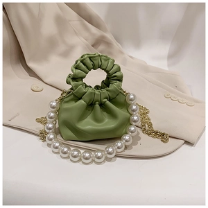 Detail of green ruched mini bag with pearl handle and gold chain on beige blazer