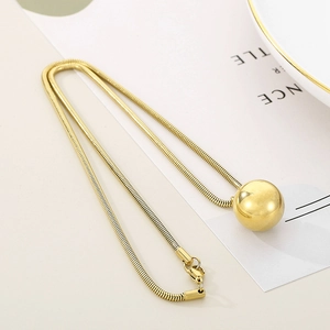 Macro detail of golden snake chain necklace with smooth metal ball pendant close-up
