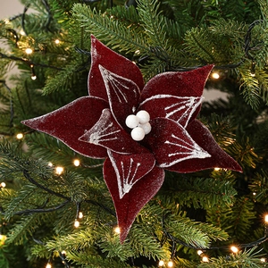 Velvet burgundy Christmas poinsettia with silver glitter edges on a green tree branch