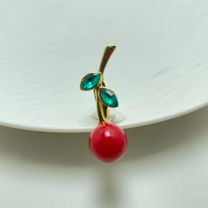 Close-up of cherry brooch with red spheres and green gemstones on white porcelain