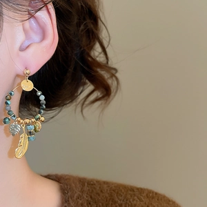 Close-up of bohemian gold feather and teal bead hoop earrings worn by a model