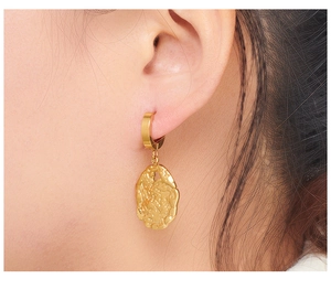 Detail of gold oval hoop earrings with textured finish worn on ear by a model