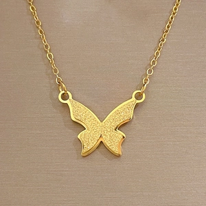 Détail macro d'un pendentif papillon doré mat avec une finition sablée délicate