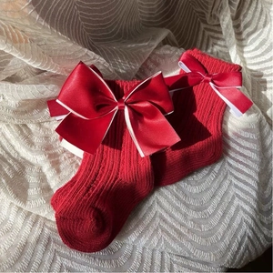 Red baby knit socks with large satin bows and white piping on cream lace backdrop