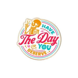 Detail of round enamel pin featuring skeleton hand and HAVE THE DAY YOU DESERVE quote