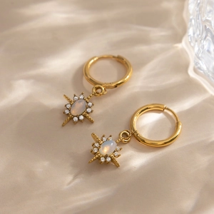Detailed shot of gold hoop earrings with opal star pendants on wavy beige silk fabric