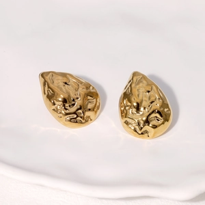 Boucles d'oreilles gouttes dorées à texture martelée sur plateau blanc, vue de studio