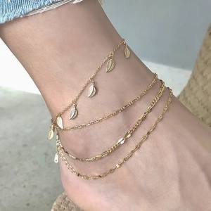 Detailed view of multilayer gold anklet featuring delicate leaf pendants on a woman's ankle