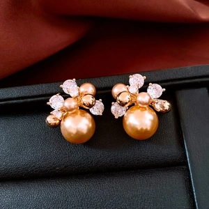 Detailed close-up of golden pearl stud earrings with zircon inlay on black surface