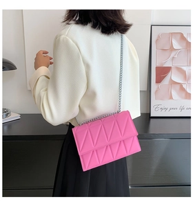 Detail of a bright pink quilted chain bag worn by a model in a modern minimalist room