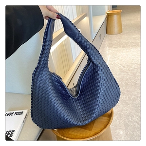 Detail of navy blue woven shoulder bag with zipper closure held against a modern interior