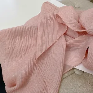 Dettaglio di una sciarpa plissettata rosa chiaro con fili lucidi in ambiente accogliente
