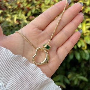 18K gold plated necklace with green gemstone cube and heart pendant held by a hand