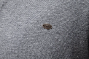 Macro shot of knit fabric texture and bronze metal logo plaque on a men cardigan sweater