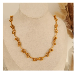 Close-up of a gold wavy chunky chain necklace with spheres on a beige jewelry display