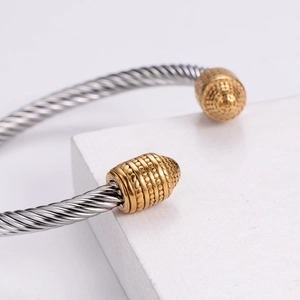 Two-tone stainless steel cable bangle with gold engraved end caps and twisted rope design