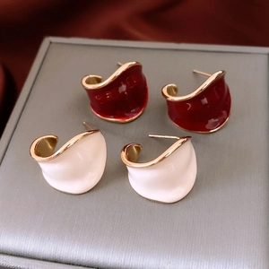 Macro detail of vintage C-shape earrings in burgundy and cream enamel with gold plating
