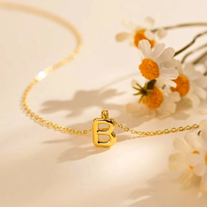 Fashionable gold bubble letter B necklace with minimalist thin chain on floral backdrop