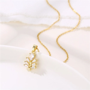 Minimalist gold leaf pendant necklace with clear zircon stones on a white background