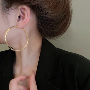 Close-up of a model wearing large gold matte textured hoop earrings in a minimalist design