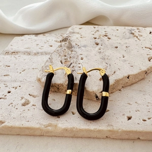 Macro detail of U-shaped gold earrings with black enamel on a natural stone and silk texture