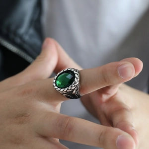 Detailed close-up of a men's stainless steel ring with a large oval green gemstone and woven texture
