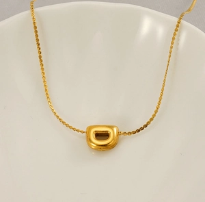 Macro shot of 18K gold plated D-letter pendant necklace inside a white porcelain bowl