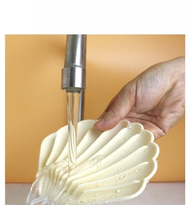 Detailed view of beige shell shaped silicone soap dish being rinsed under running water