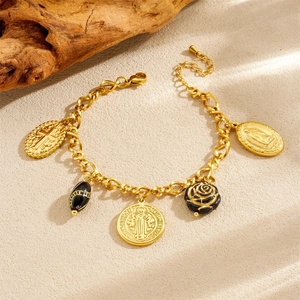 Gold stainless steel bracelet with cross, black rose, and medal charms on beach sand