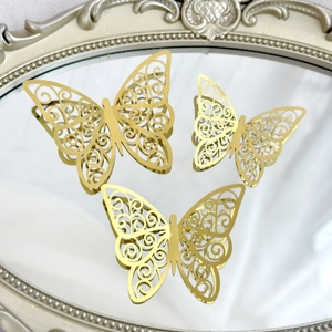 Three gold 3D hollow butterfly decorations with metallic finish on a vintage mirror