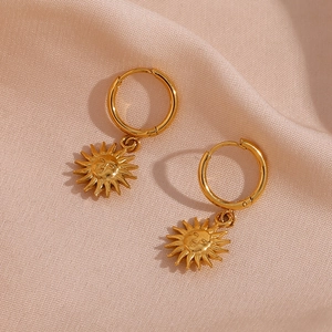 Golden stainless steel sun face hoop earrings on smooth silk fabric background