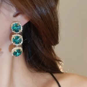 Close-up of elegant gold earrings with three green gemstones and diamond accents on model