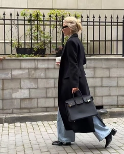 Chic long black wool coat styled with blue jeans and leather handbag in street view