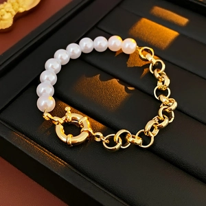 Dettaglio del bracciale con perle e catena dorata con chiusura a molla su vassoio in pelle