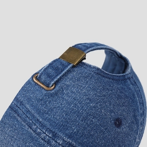 Detail of adjustable brass buckle on washed blue denim baseball cap showing premium stitching